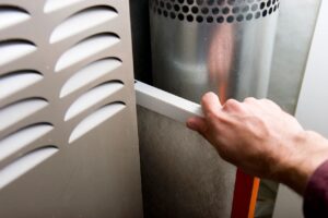 Hand adjusting a filter in an HVAC system, highlighting air conditioning maintenance relevant to spring upkeep in Noblesville, IN.