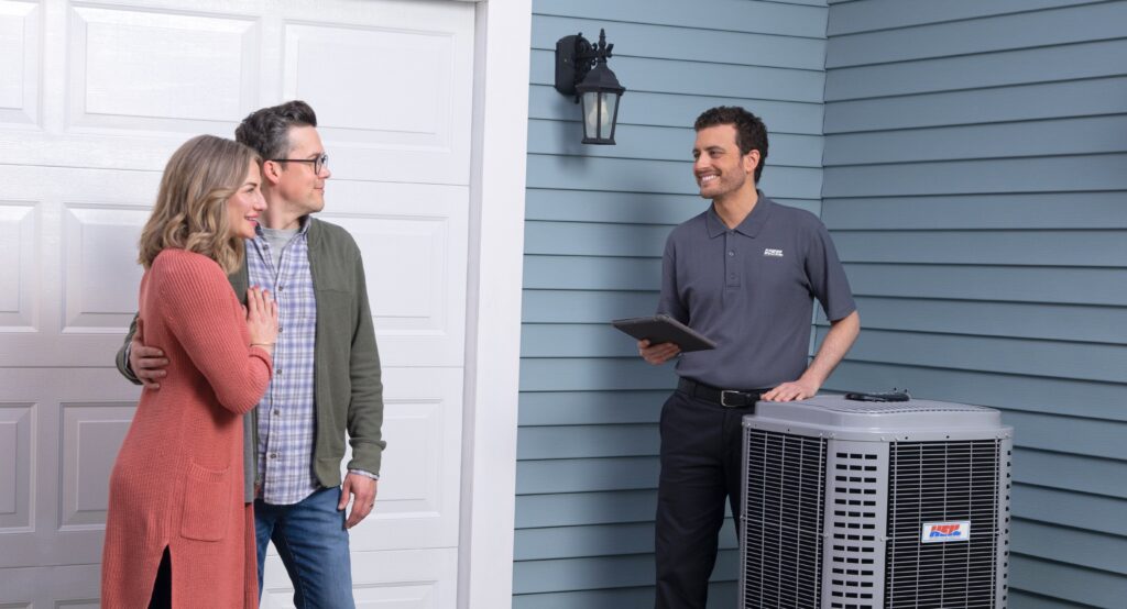Couple discussing HVAC service with technician near air conditioning unit, emphasizing importance of regular maintenance in Indiana.